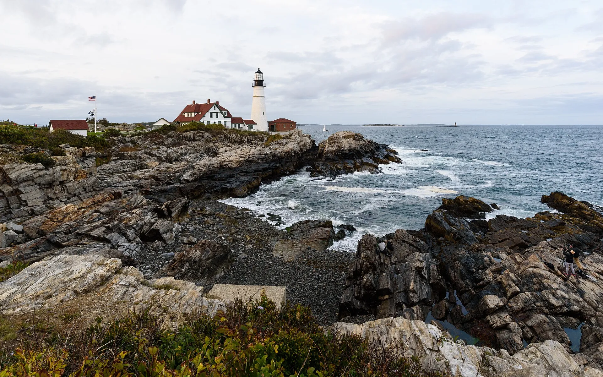 Portland Head Light and the keeper's house above the ledges at Fort Williams Park, with Ram Island Ledge Light visible offshore.