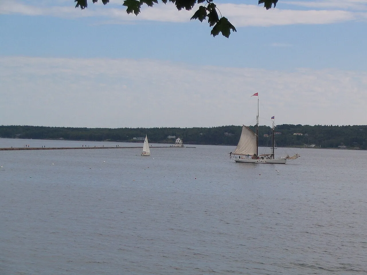 Rockland Harbor with the granite breakwater running out to the small white lighthouse, walkers along it, and a schooner under sail
