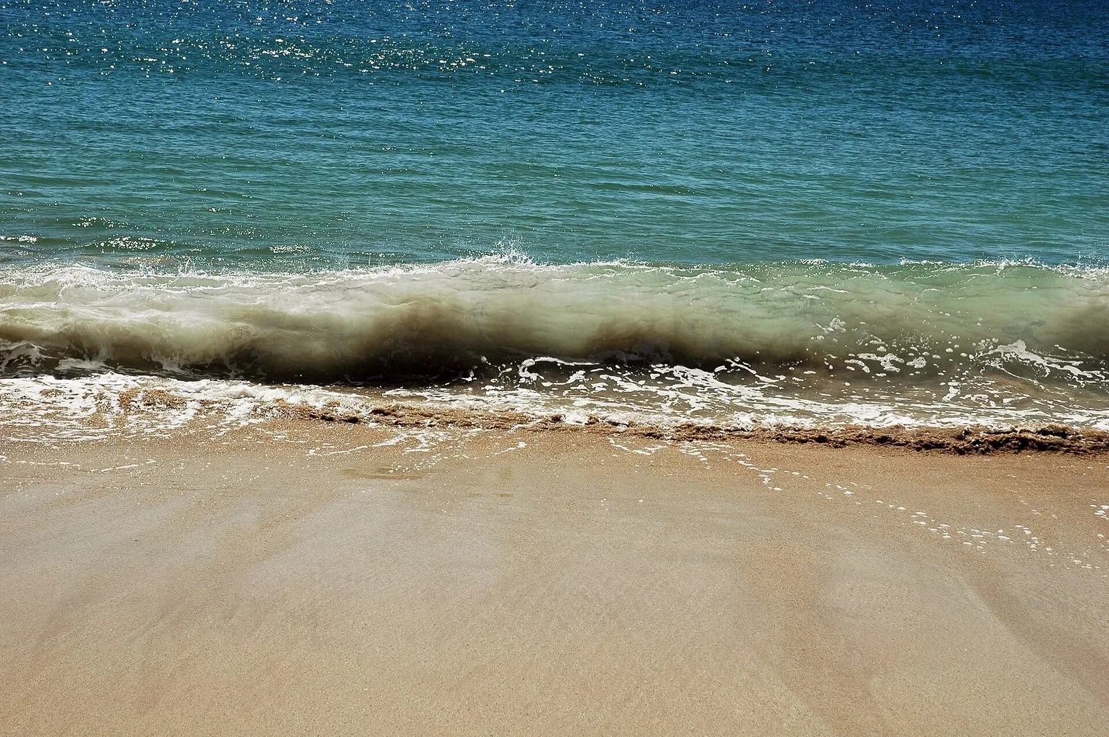 A wave curling over and breaking onto flat sand